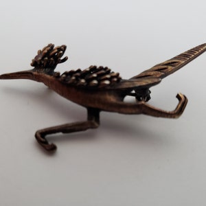 Może przedstawiać: Bransoletka z brązowego metalu w kształcie bielika z detalicznymi skrzydłami i nogami. Ptak jest przedstawiony w locie z głową zwróconą w bok.