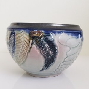 May include: A white ceramic bowl with a blue rim and a raised design of leaves in shades of blue, green, and brown.