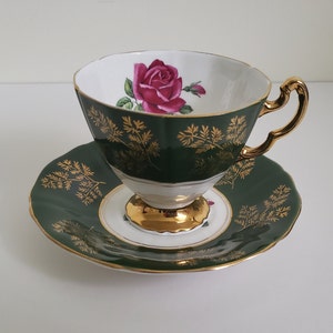 Peut inclure: Une tasse à thé et une soucoupe en vert et or avec un motif de rose rose. La tasse à thé a un bord doré et une base dorée. La soucoupe a un bord doré et un motif doré.