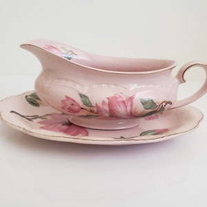 May include: A pink porcelain gravy boat with a matching saucer. Both pieces feature a floral design with pink and green magnolia blossoms.