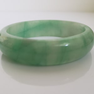 May include: A green jade bangle bracelet. The bracelet is smooth and polished, with a light green color.