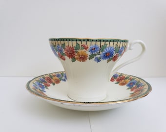 May include: A vintage teacup and saucer set with a floral pattern. The cup and saucer are white with a yellow background and a border of blue, red, and yellow flowers. The border also has a green and gold trim.