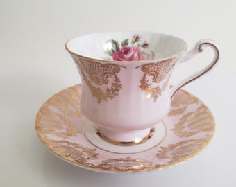 May include: A pink teacup and saucer set with gold trim and a floral design. The cup has a delicate handle and the saucer has a scalloped edge.