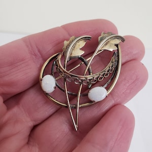Op de afbeelding: Een broche van goudkleurig metaal met twee gestileerde bladeren en drie witte opalen.