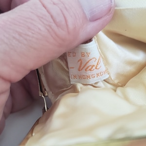 Pu&ograve; includere: Una borsa in tessuto di raso bianco con un'etichetta che recita "Made by -Val- in Hong Kong".