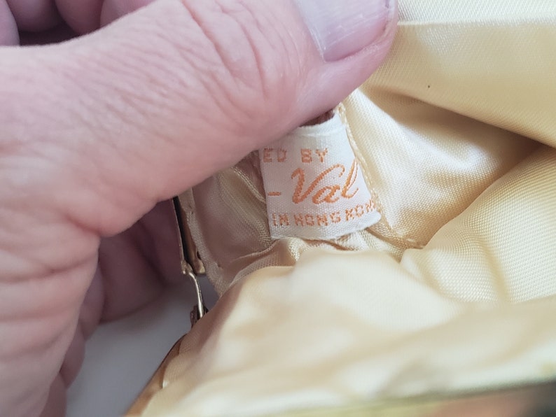 Pu&ograve; includere: Una borsa in tessuto di raso bianco con un'etichetta che recita "Made by -Val- in Hong Kong".