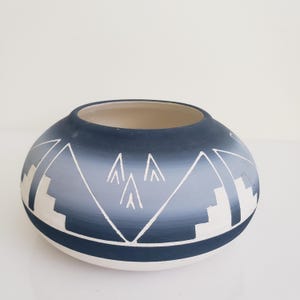 May include: A spherical ceramic vase with a broad opening. The vase features a gradient of blue tones, transitioning from dark navy at the top to a lighter shade at the base. White geometric designs, including triangles and stepped patterns, decorate the exterior.