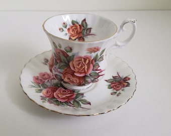 Puede incluir: Un juego de taza y platillo de té blanco con un patrón floral de rosas rosas y naranjas. El juego tiene un borde dorado.