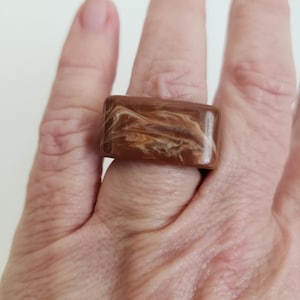 May include: A brown and white marbled rectangular ring. The ring is made of resin and has a swirled pattern.