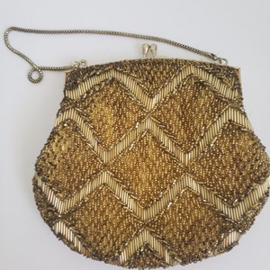 Pu&ograve; includere: Una borsa da sera in perline dorate con un motivo a chevron. La borsa ha una tracolla a catena argentata.