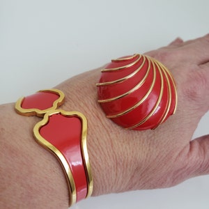 May include: A red and gold bangle bracelet with a curved design and a matching red and gold brooch with a swirl pattern.