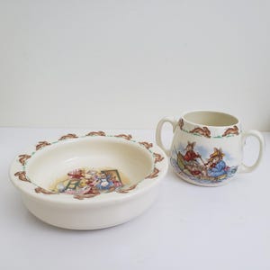 以下が含まれることがあります： クリーム色のセラミックボウルとマグカップのセット。ボウルは茶色のウサギで装飾された広い縁と中央のイラストがあります。マグカップは2つのハンドルと、同様のウサギのデザイン、ボートシーンのイラストが特徴です。