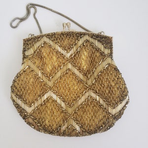 Pu&ograve; includere: Una borsa da sera in perline dorate con una tracolla a catena. La borsa ha un motivo a chevron.