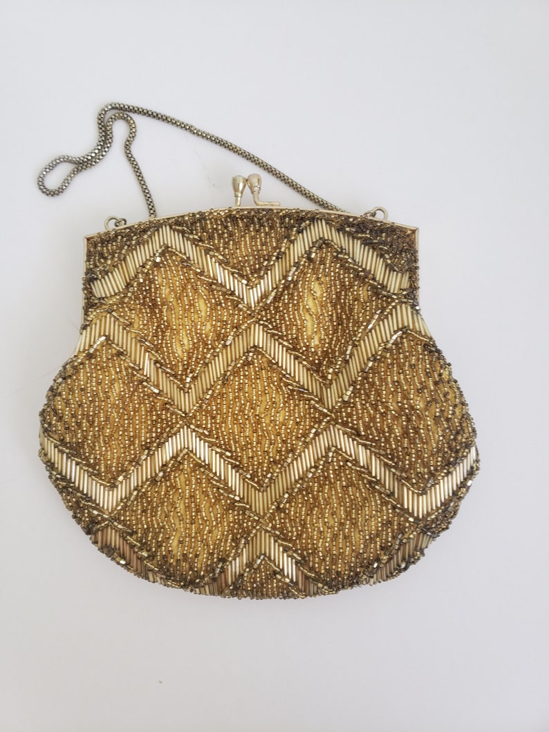 Pu&ograve; includere: Una borsa da sera in perline dorate con una tracolla a catena. La borsa ha un motivo a chevron.