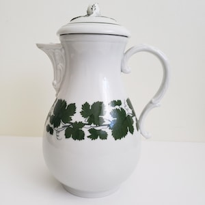 May include: White porcelain coffee pot with a green vine design and a lid. The pot has a rounded body and a handle.