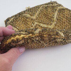 Pu&ograve; includere: Una pochette da sera in perle dorate con un motivo decorativo. La pochette &egrave; realizzata con piccole perle rotonde cucite insieme per creare una superficie testurizzata.