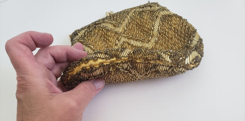 Pu&ograve; includere: Una pochette da sera in perle dorate con un motivo decorativo. La pochette &egrave; realizzata con piccole perle rotonde cucite insieme per creare una superficie testurizzata.