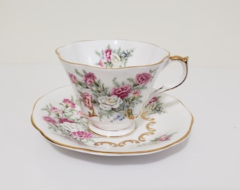Può includere: Servizio da tè bianco con tazza e piattino decorati con un motivo floreale di fiori rosa, bianchi e viola. I bordi della tazza e del piattino sono dorati. La tazza ha un manico curvo.