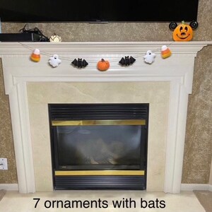 May include: A Halloween garland with seven felt ornaments, including bats, pumpkins, ghosts, and candy corn. The garland is hanging above a fireplace.