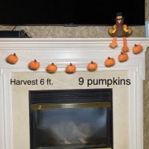 May include: A garland of nine orange felt pumpkins strung on a twine cord. The garland is 6 feet long and is displayed on a white mantel above a fireplace. The text "Harvest 6 ft." and "9 pumpkins" is written below the garland.