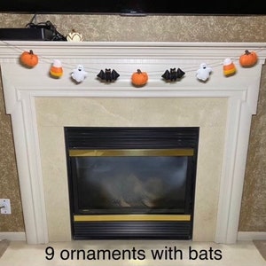 May include: A Halloween garland with nine felt ornaments, including pumpkins, bats, ghosts, and candy corn, hanging above a fireplace.