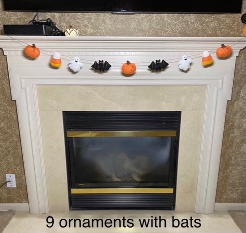 May include: A Halloween garland with nine felt ornaments, including pumpkins, bats, ghosts, and candy corn, hanging above a fireplace.