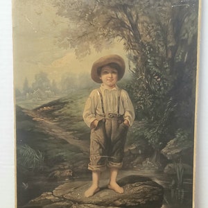 May include: Vintage framed print of a young child standing on a rock near a stream. The child wears a hat, suspenders, and knickerbockers. The background features a landscape with trees and a small building. The print has a sepia tone.