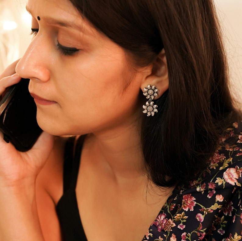 May include: A pair of silver dangle earrings with two flower-shaped charms. Each charm is adorned with small, clear rhinestones.