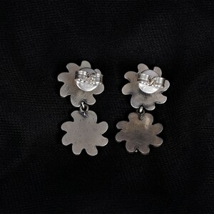 May include: A pair of silver dangle earrings with a flower design. The earrings have a post back closure.