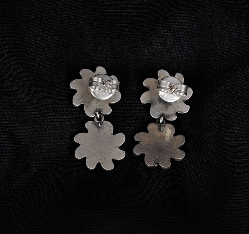 May include: A pair of silver dangle earrings with a flower design. The earrings have a post back closure.