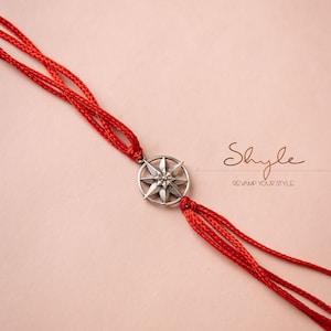 Puede incluir: Un brazalete de cuerda roja con un dije de estrella de plata. El dije está en el centro del brazalete y tiene un diseño de estrella. El brazalete está sobre un fondo rosa. El texto "Shyle Revamp Your Style" está en la esquina superior derecha de la imagen.