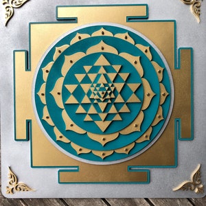 May include: A teal blue and gold Sri Yantra mandala with a geometric design. The mandala is surrounded by a gold frame and is set against a white background.