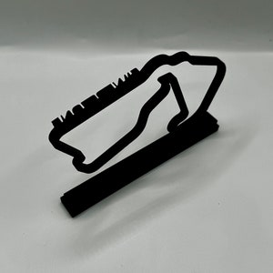 May include: Black metal model of a race track, with a raised base. The track is shaped like a figure eight.