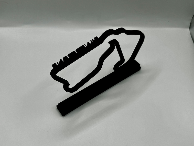 May include: Black metal model of a race track, with a raised base. The track is shaped like a figure eight.