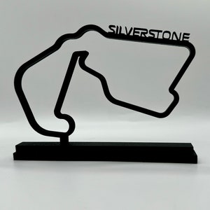 May include: Black 3D model of the Silverstone race track on a black base. The track is a stylized outline of the circuit with the word "SILVERSTONE" printed above it.