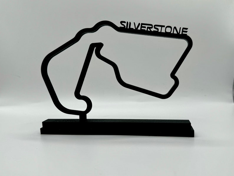 May include: Black 3D model of the Silverstone race track on a black base. The track is a stylized outline of the circuit with the word "SILVERSTONE" printed above it.