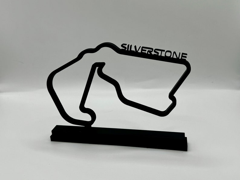 May include: Black metal model of the Silverstone racetrack with the name "SILVERSTONE" printed on the track. The model is on a black base.