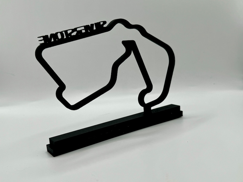 May include: Black 3D printed model of the Monza race track with the word "MONZA" printed on the top. The model is on a black base.