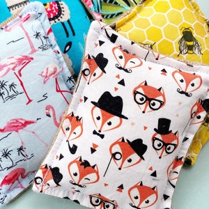 May include: Close-up of several square fabric items with various patterns. One features pink flamingos on a light blue background. Another has orange foxes with hats and glasses on a white background. Other patterns include a llama and a honeycomb with a bee.