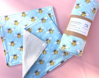 May include: Reusable kitchen roll and two matching washcloths. The roll and cloths feature a light blue background with a repeating pattern of yellow and black bees. The washcloths have a white terry cloth backing and snap closures. The roll is wrapped in brown paper.