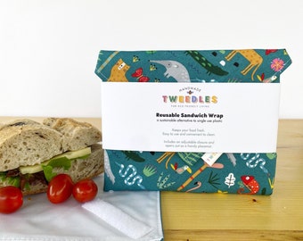 May include: A reusable sandwich wrap with a teal background and a colorful animal print. The wrap is folded and held together with a white band that reads "Reusable Sandwich Wrap". A sandwich and tomatoes are next to the wrap.