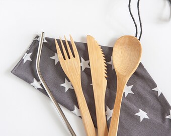 May include: A reusable cutlery set includes a stainless steel straw, a bamboo fork, knife, and spoon. The utensils rest on a gray fabric pouch with white star patterns. A black cord is attached to the pouch.