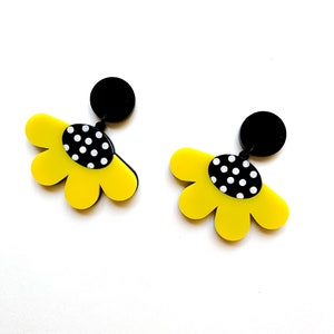 May include: A pair of yellow flower-shaped earrings with black polka dot centers and black posts.