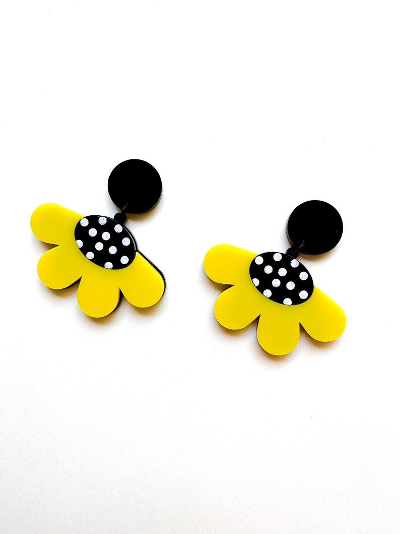 May include: A pair of yellow flower-shaped earrings with black polka dot centers and black posts.
