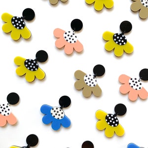 May include: A set of 12 colorful flower-shaped earrings with black polka dots. The earrings are made of acrylic and have a black post.