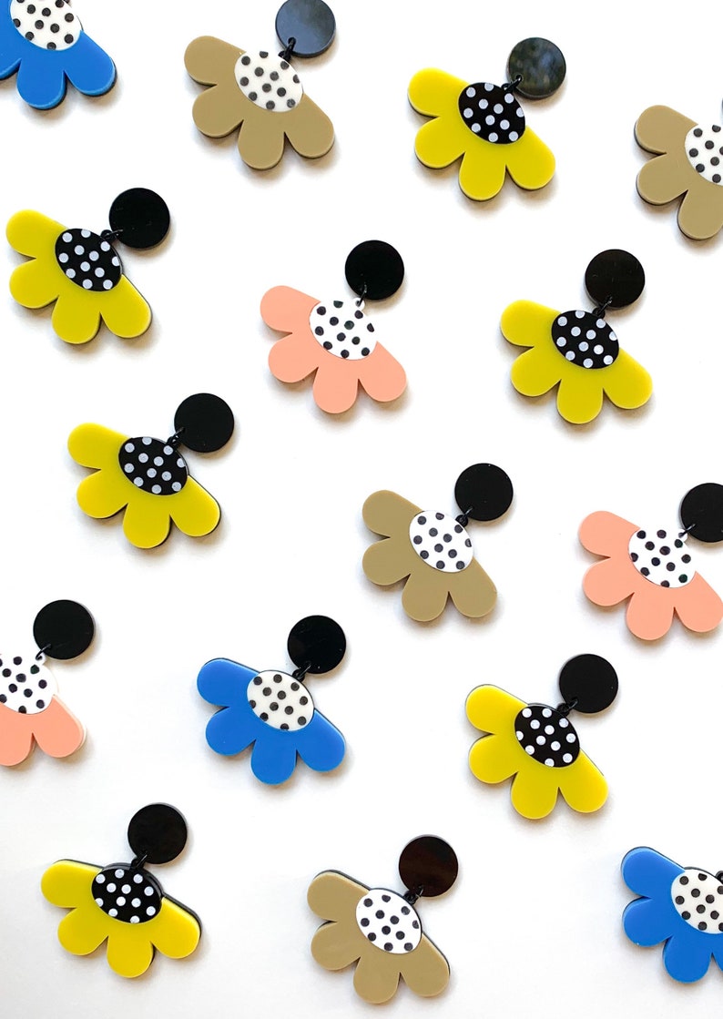 May include: A set of 12 colorful flower-shaped earrings with black polka dots. The earrings are made of acrylic and have a black post.
