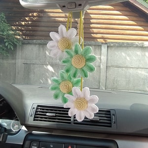 May include: A car interior with a rearview mirror and a string of crocheted white and green daisy flowers hanging from it.