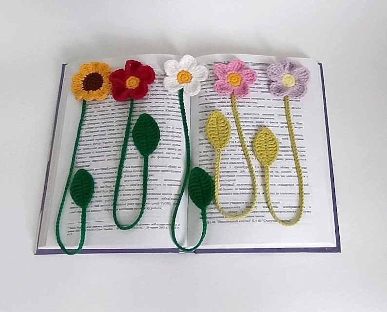 May include: Five crocheted flower bookmarks with green stems and leaves. The flowers are yellow, red, white, pink, and purple.
