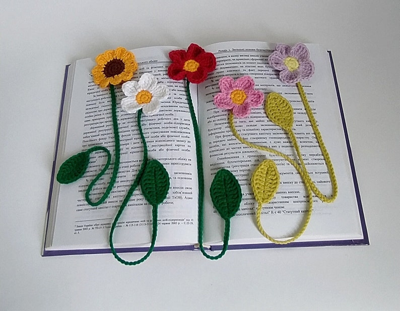 May include: Five crocheted flower bookmarks with green leaves. The flowers are yellow, white, red, pink, and purple.