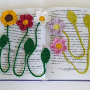 May include: Five crocheted flower bookmarks in different colors, including yellow, red, white, purple, and pink. The bookmarks are attached to a book with the text "Pravila 1. Znachnost' vliyaniya faktorov" visible.